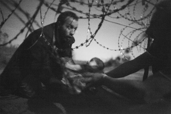 A grande vencedora deste ano na premiação da WWP é esta imagem que mostra um homem passando um bebê para uma outra pessoa por baixo de uma cerca de arame farpado. A foto foi registrada pelo australiano Warren Richardson no dia 28 de agosto de 2015, na fronteira entre a Sérvia e a Hungria. Segundo o fotógrafo, que acampou com os refugiados, essas pessoas tentavam chegar na Hungria antes que a cerca de segurança estivesse concluída (Crédito foto: Warren Richardson/World Press Photo 2016).