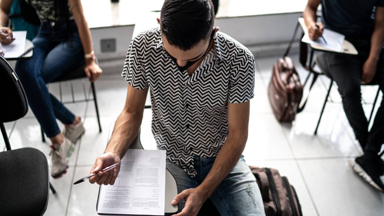 Estudante concentrado fazendo anotações ou fazendo um teste em uma universidade - usando máscara facial