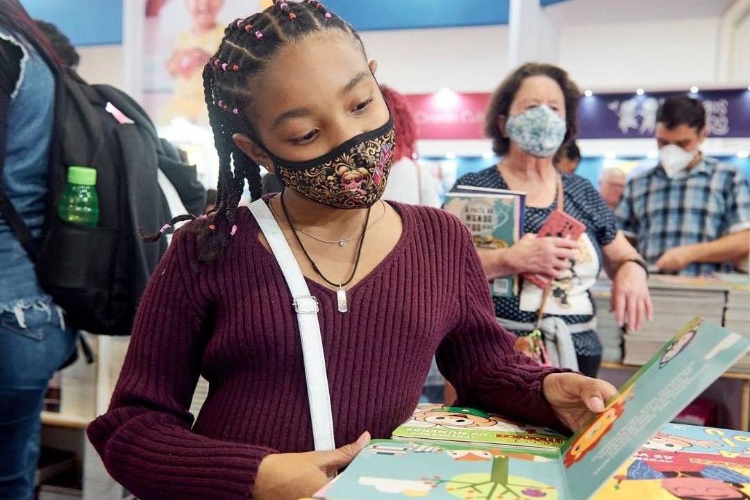 Menina negra folheia um livro na Bienal Internacional do Livro de São Paulo.