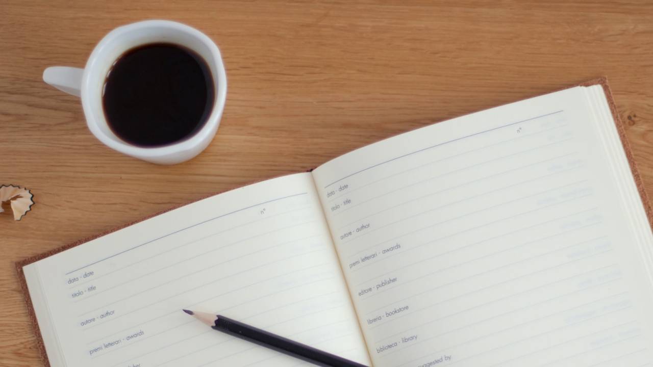 Mesa; estudos; caderno; café; xícara de café ao lado de caderno e lápis preto