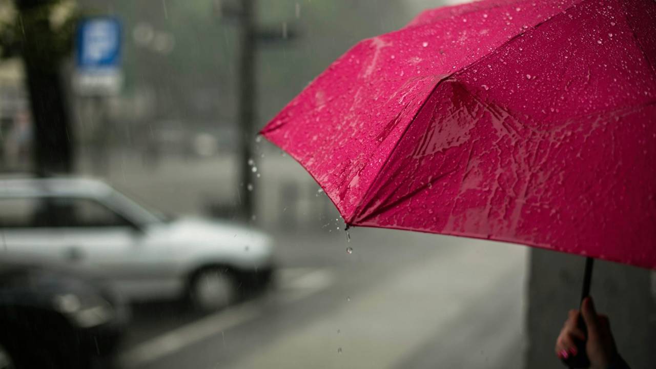 Pessoa segura guarda-chuva vermelho em meio à cidade chuvosa
