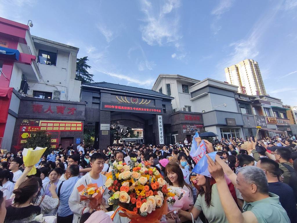 estudantes-gaokao Multidão em frente a escola, alguns seguram buquês de flores