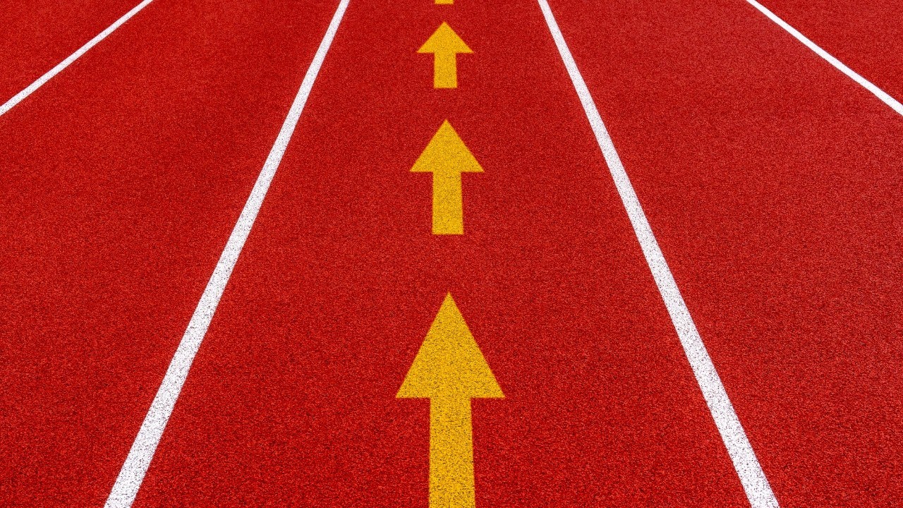 Pista de corrida vermelha com três setas amarelas apontando para frente, indicando progresso ou direção, e duas linhas brancas laterais